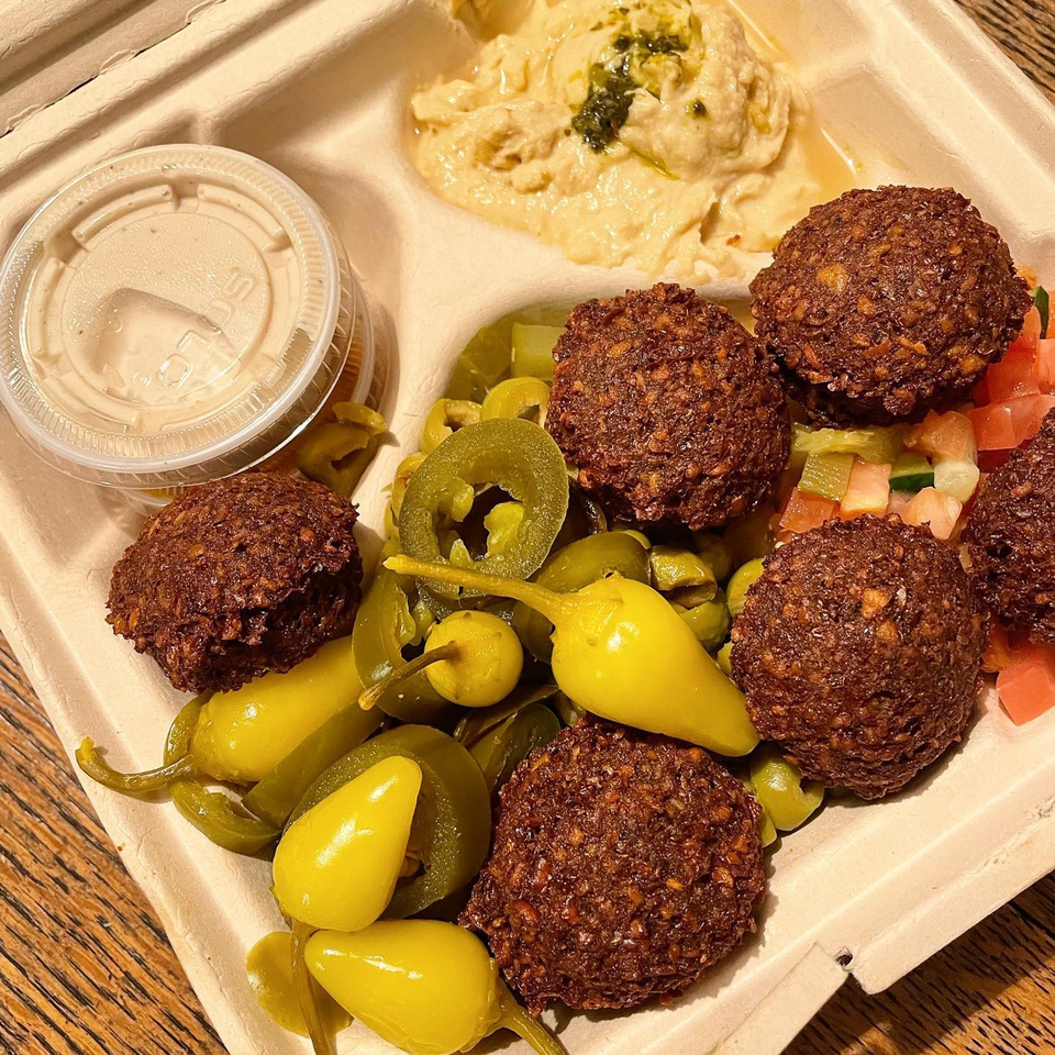 Mordy's Corner falafel platter with hummus, pickled peppers, and chopped salad in a to-go container.
