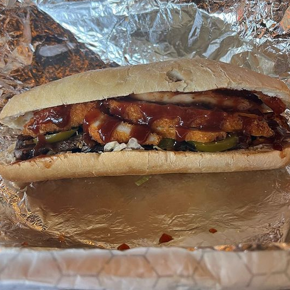 A large kosher sandwich from Mordy's Corner, filled with meat, crispy chicken, pickles, and BBQ sauce.