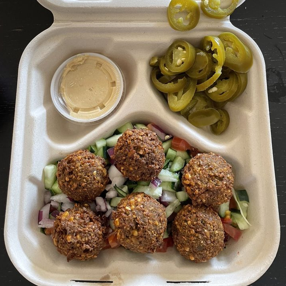 Kosher falafel with chopped salad, pickled jalapeños, and tahini sauce in a takeout container.