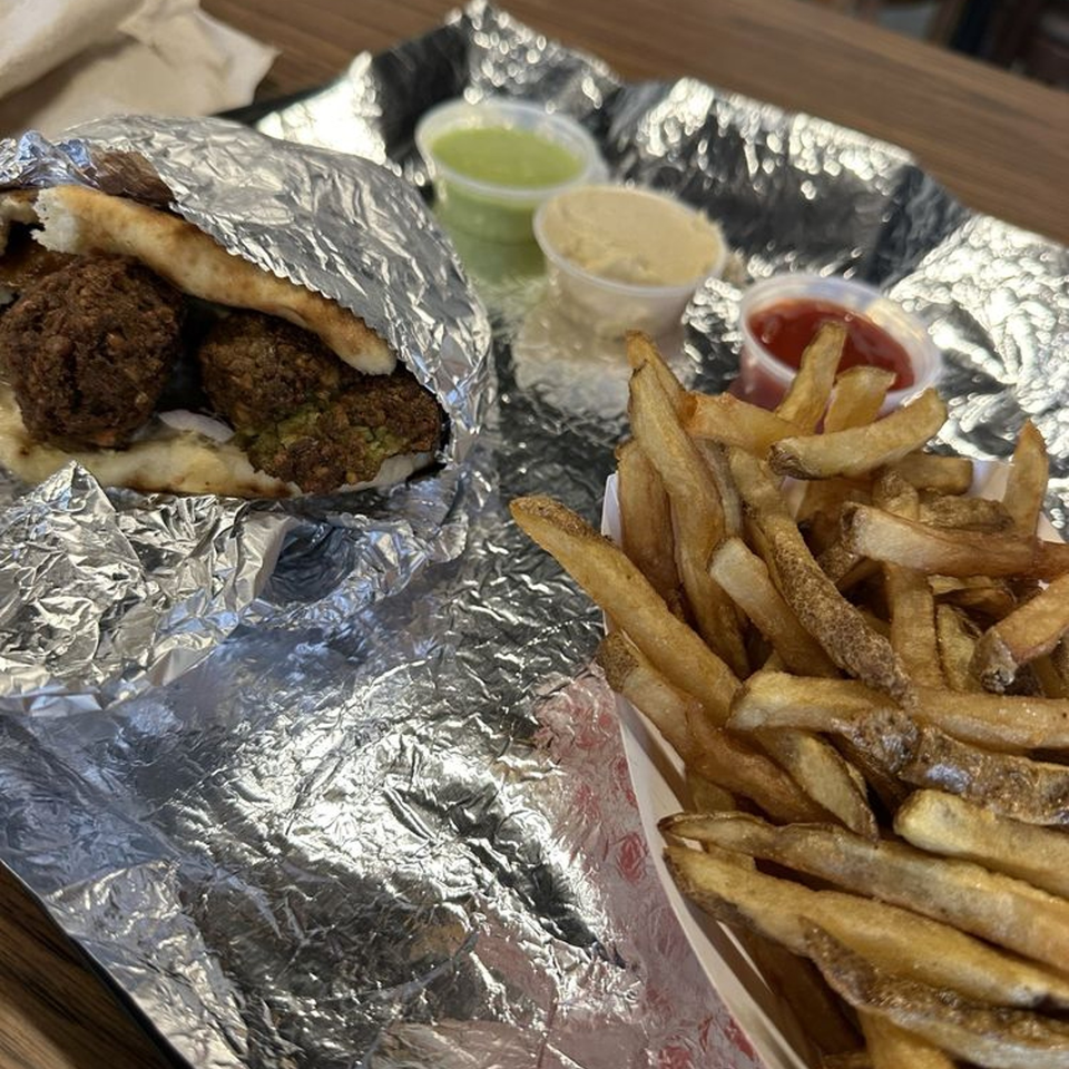Mordy's Corner falafel pita wrapped in foil, with a side of fries and dipping sauces.